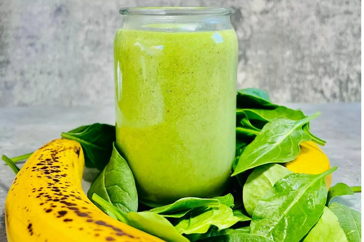a side shot of kiwi smoothie surrounded by spinach and bananas