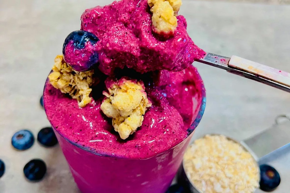 a spoonful of thick blueberry smoothie with granola on a glass cup