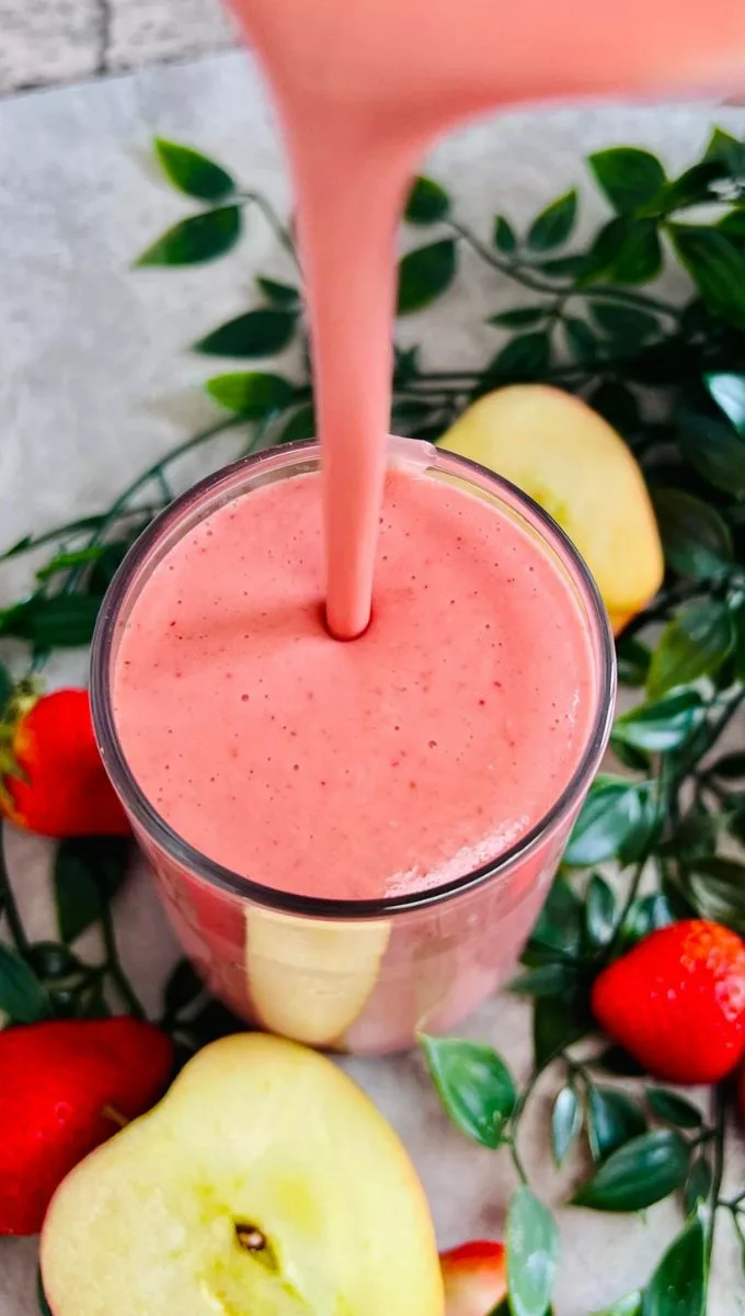 Apple Strawberry Smoothie being poured into a thin glass cup from a blender