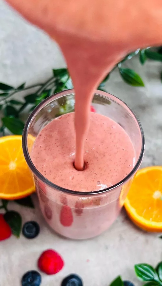 Energy-Boosting Smoothie being poured into a tall thin glass cup from a blender jug