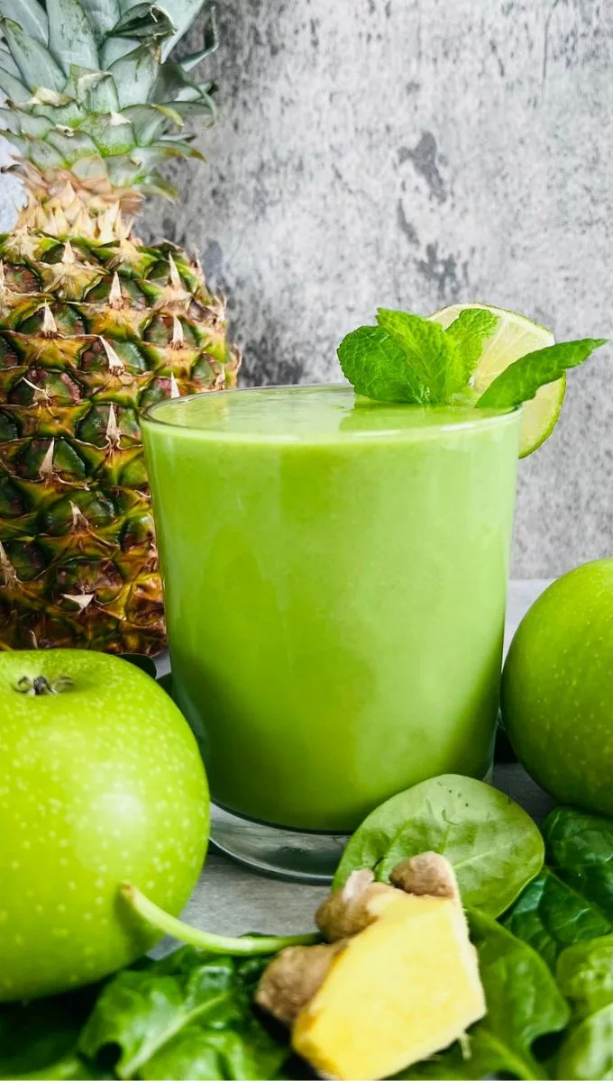 Green Apple Ginger Smoothie surrounded by leaves, green apple, and pineapple
