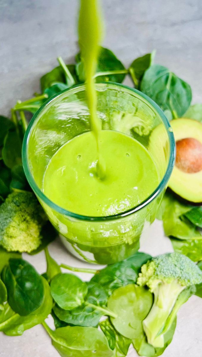 Green Broccoli Smoothie being poured into a tall thin glass cup from a blender jug
