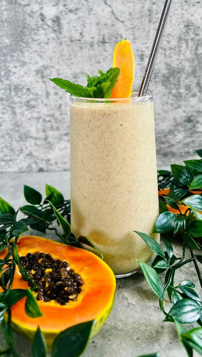Papaya Pineapple Smoothie surrounded by greens mint and fresh slliced papaya