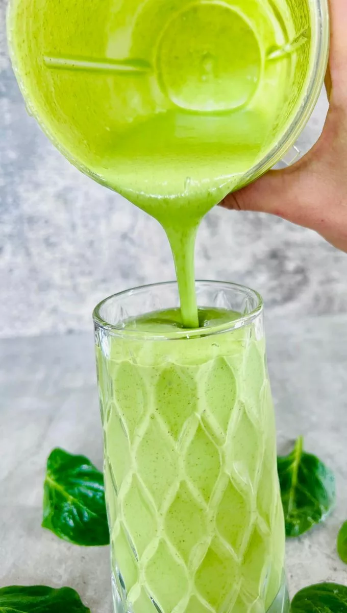Spinach Protein Smoothie being poured into a thick tall glass cup from a blender jug