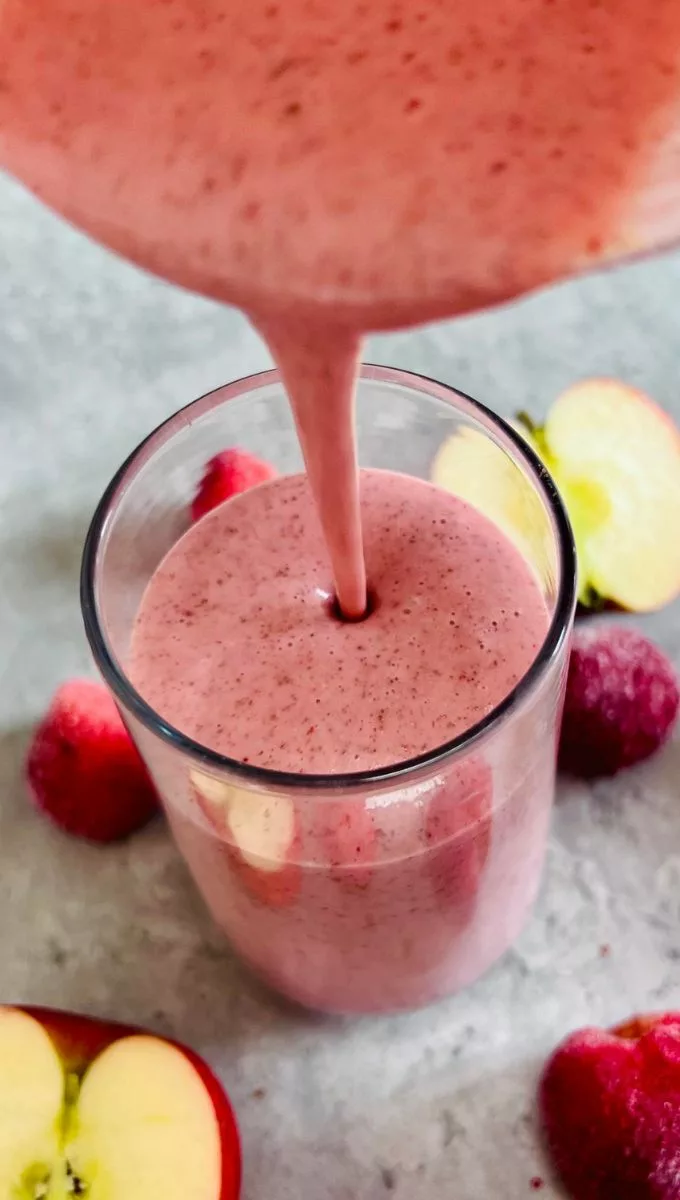Strawberry Apple Banana Smoothie being poured into a tall thin glass cup from a blender jug