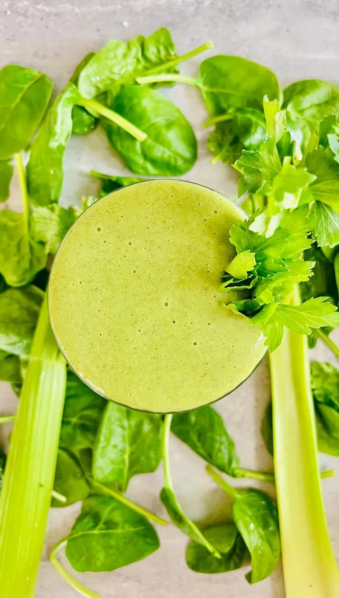 a green celery smoothie for weight loss surounded by spinach leaves
