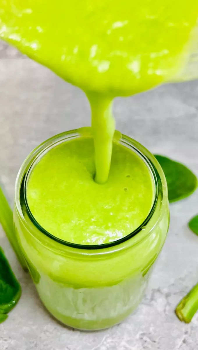 green celery smoothie being poured into a glass cup