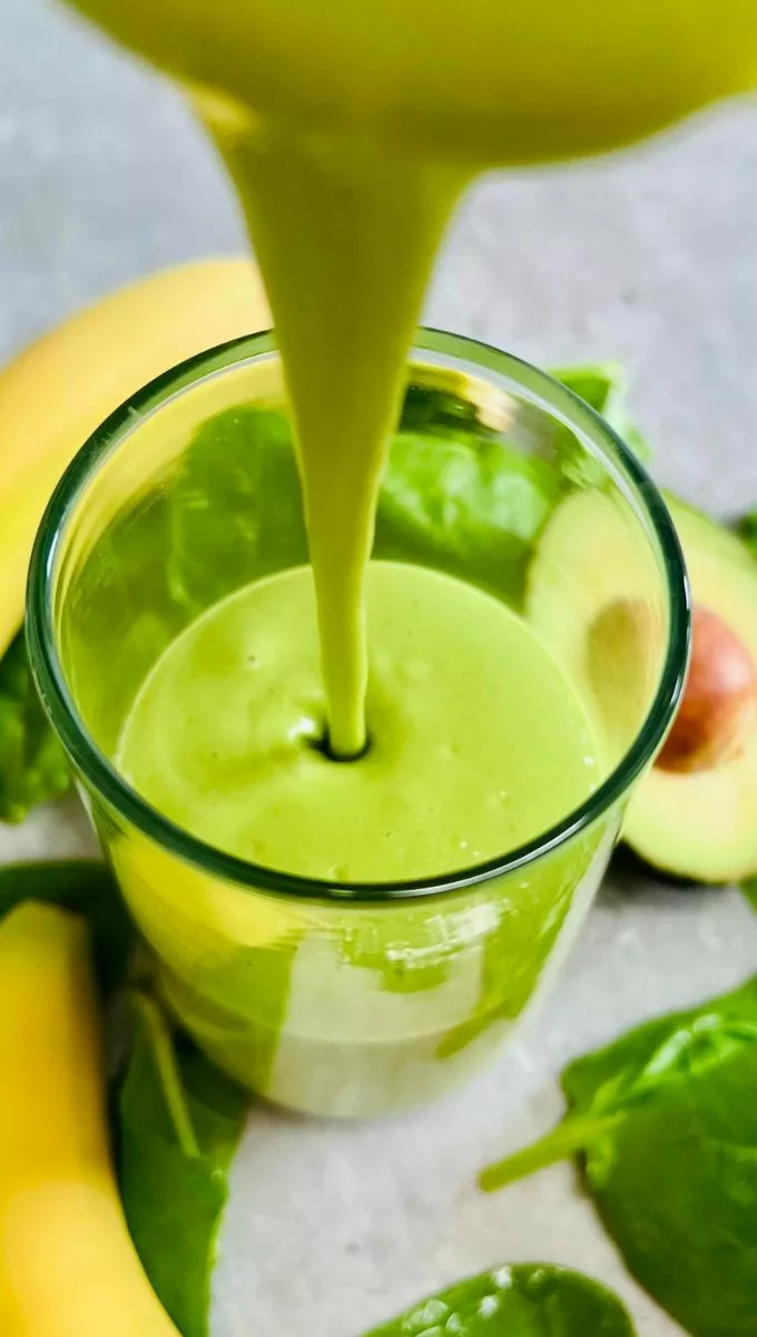Banana Avocado Smoothie being poured into a thin glass cup from a blender