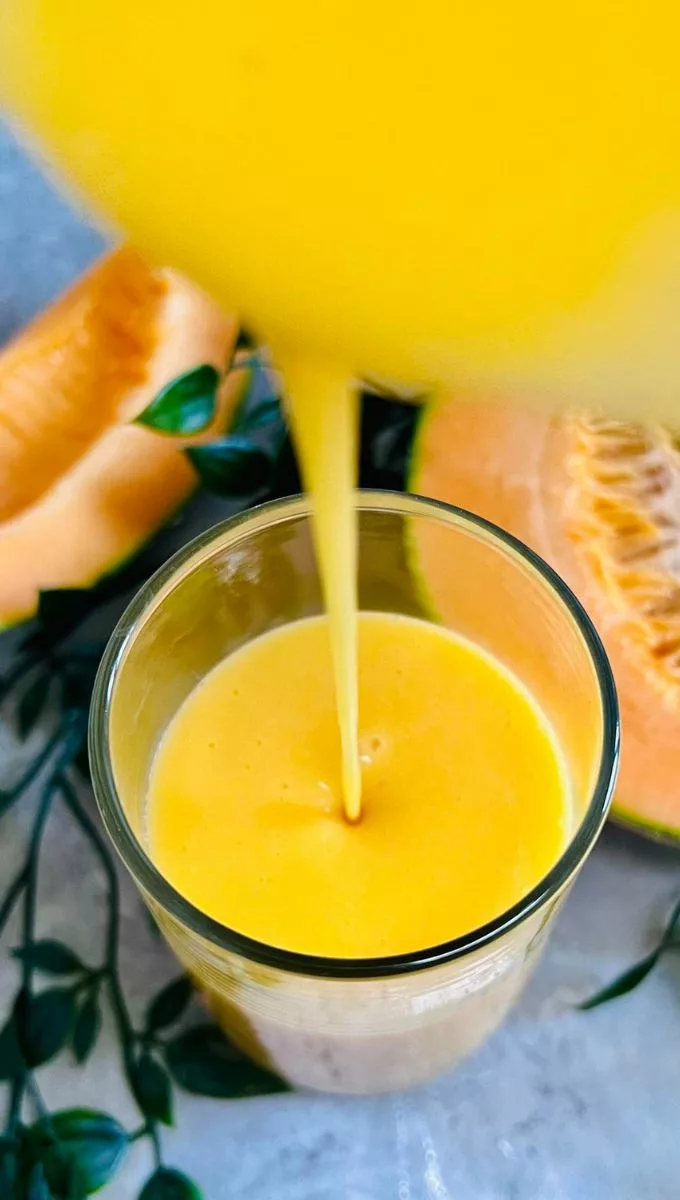 Cantaloupe Smoothie being poured into a tall thin glass cup from a blender jug