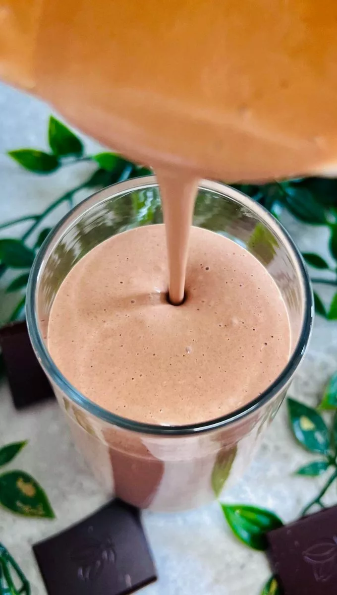 Chocolate Peanut Butter Banana Smoothie being poured into a tall thin glass cup from a blender jug