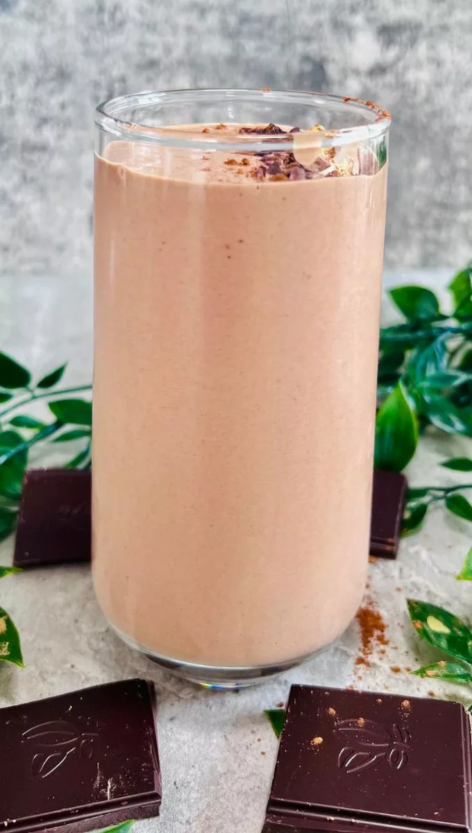 Chocolate Peanut Butter Banana Smoothie served in a tall thin glass cup surrounded by chocolate squares and greens