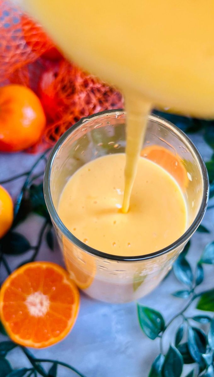 Clementine Smoothie being poured into a tall thin glass cup from a blender jug
