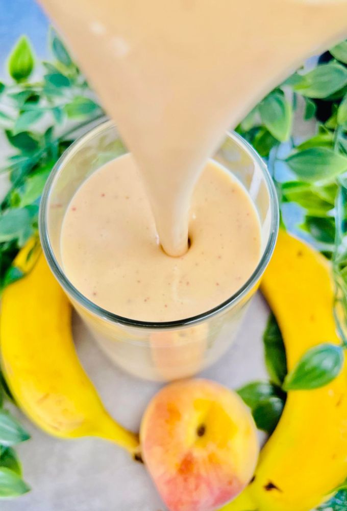 Peach Banana Smoothie being poured into a tall thin glass cup from a blender jug